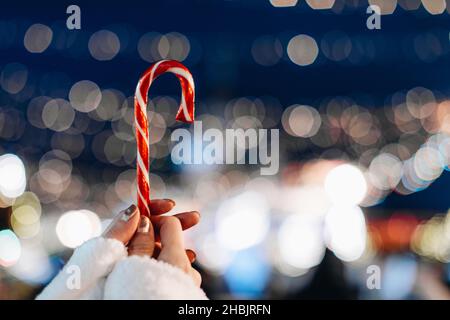 Mains femelles tenant rouge blanc canne sucrée lolipop sur le fond de bleu argent magie illumination.Détails de la fée de Noël Banque D'Images