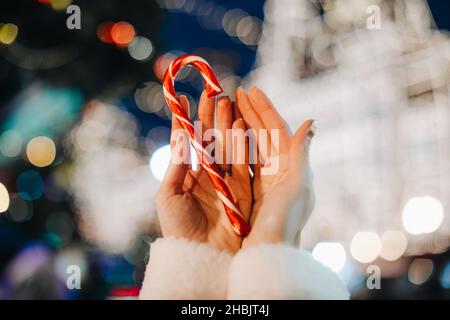 Mains femelles tenant rouge blanc canne sucrée lolipop sur le fond de bleu argent magie illumination.Détails de la fée de Noël Banque D'Images