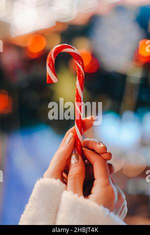 Mains de femmes tenant rouge blanc canne sucrée lolipop sur le fond de bleu bokeh lumière.Détails de la fée de Noël Banque D'Images