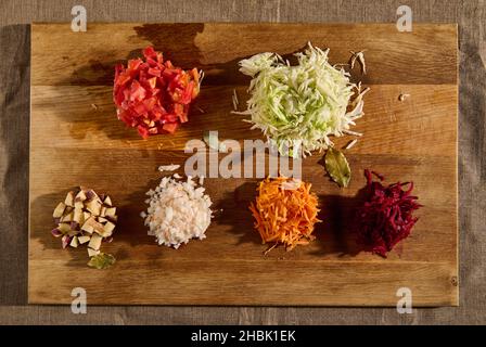 Légumes frais hachés et râpés - betteraves, oignons de carottes, tomates, pommes de terre et chou sur une planche à découper en bois.Pose plate d'ingrédients hachés Banque D'Images