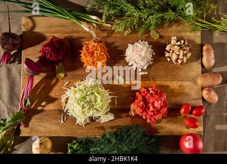 Légumes crus hachés - betteraves, oignons de carottes, tomates, pommes de terre, chou et aneth frais vert humide sur une planche à découper en bois.Couche plate de lingre hachée Banque D'Images