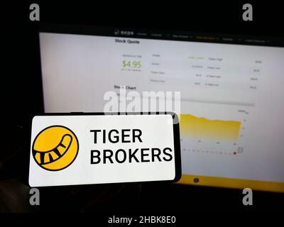Personne tenant le téléphone portable avec le logo de la société FINTECH Holding Limited (Tiger Brokers) à l'écran devant la page web.Mise au point sur l'affichage du téléphone. Banque D'Images