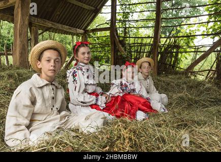 Salaj, Roumanie - 15 mai 2018 : jeunes filles et garçons ruraux vêtus de costumes traditionnels assis dans un hanyloft au moment de la récolte à la campagne Banque D'Images