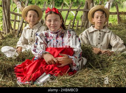 Salaj, Roumanie - 15 mai 2018 : jeunes filles et garçons ruraux vêtus de costumes traditionnels assis dans un hanyloft au moment de la récolte à la campagne Banque D'Images