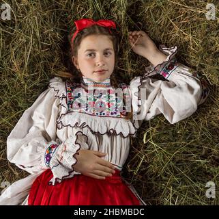 Salaj, Roumanie - 15 mai 2018 : jeune fille rurale vêtue de costumes traditionnels assis dans un hanyloft au moment de la récolte à la campagne Banque D'Images