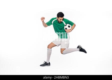 jeune joueur de football en uniforme sautant avec le ballon de football sur blanc Banque D'Images