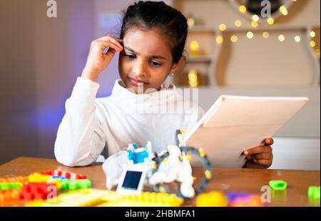 Une jeune fille réfléchie prépare un robot de bricolage en regardant le manuel d'instruction à la maison - concept de faire des expériences scientifiques, apprentissage de l'enfance Banque D'Images