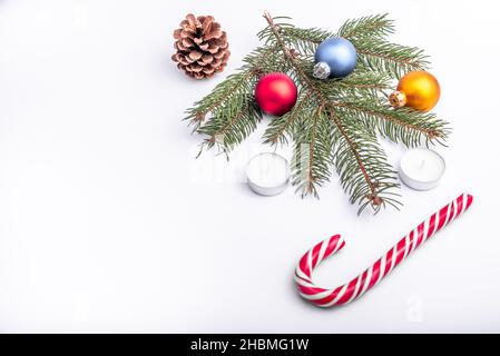 Appartement de Noël et de nouvel an : branche de sapin vert, cône, boules rouges, bleues et jaunes, deux bougies et bonbons caramel sur fond blanc isolé. Banque D'Images