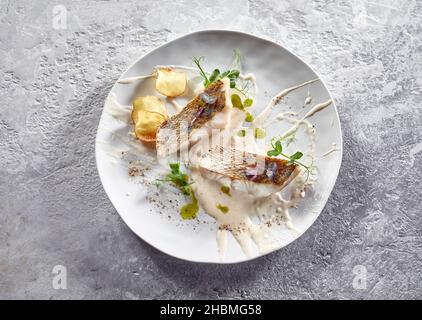 Vue de dessus de délicieux morceaux de pikeperch servis avec des tranches de pommes de terre frites et de sauce dans le restaurant de haute cuisine Banque D'Images