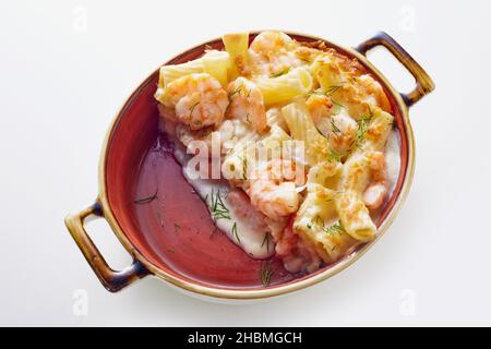 Au-dessus de l'appétissant rigatoni pâtes cuites en cocotte avec crevettes et sauce crémeuse et décorées avec des herbes sur table blanche Banque D'Images