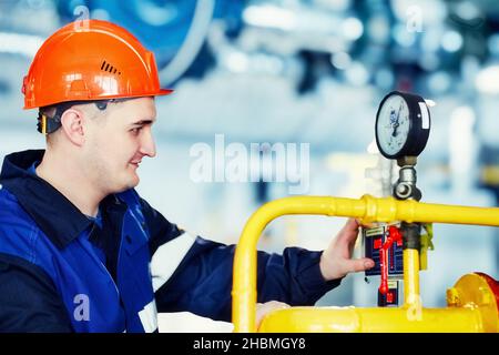 L'opérateur de la chaudière à gaz contrôle la pression sur l'équipement.Portrait d'un ingénieur en casque au travail.Flux de travail authentique. Homme travaillant dans la chaufferie.Arrière-plan flou.Gazéification et énergie.Arrière-plan. Banque D'Images