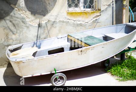 Un vieux bateau de pêche amarré par un mur de ciment avec une fenêtre.La roue se trouve sous le bateau. Banque D'Images