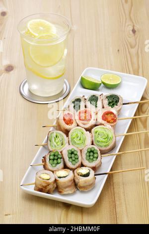 Cuisine japonaise.Les légumes enveloppés dans de la viande de porc finement tranchée sont brochés et grillés. Maïs jeune, pousses d'ail, laitue, tomates et coriandre. Banque D'Images