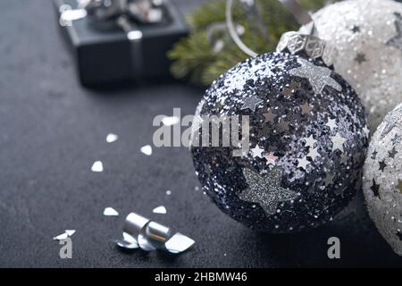 Concept de Noël ou du nouvel an avec boule de boules noires et argentées, boîte cadeau et champagne avec ruban métallique argenté décoré sur fond noir.Ha Banque D'Images