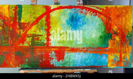Une peinture abstraite de Susanne Wiczorek sur un chevalet à Grevenbroich, en Allemagne, une arche rouge s'étendant sur des champs de vert et de bleu. Banque D'Images
