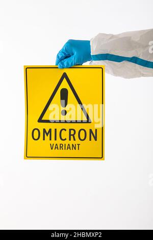 Détail d'un bras d'une infirmière médicale portant un EPI et des gants en latex avec un signe jaune avec un symbole de danger qui se lit comme suit : 'VARIANT OMICRON'.Coronavirus, Banque D'Images