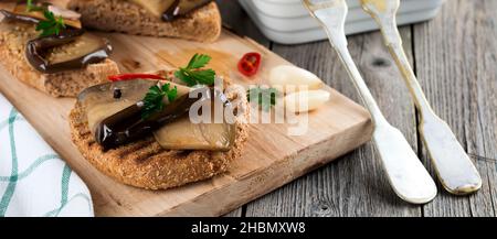 Bruschetta à l'aubergine marinée avec piment, ail et persil sur un support en bois.Mise au point sélective. Banque D'Images