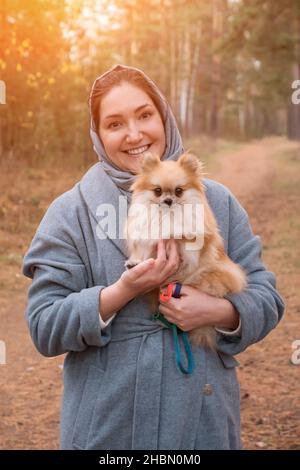 Jeune femme tenant le pomeranian mini spitz dans les bras tout en marchant dans le parc d'automne Banque D'Images