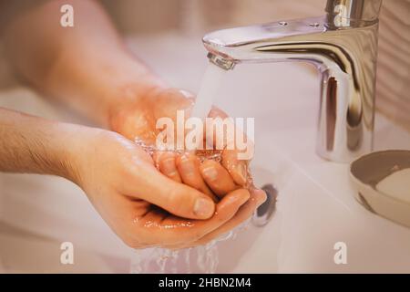 Un homme lave la mousse de ses mains sous un jet d'eau propre du robinet sur le lavabo de la salle de bains.Propreté et hygiène.Soins de santé. Banque D'Images