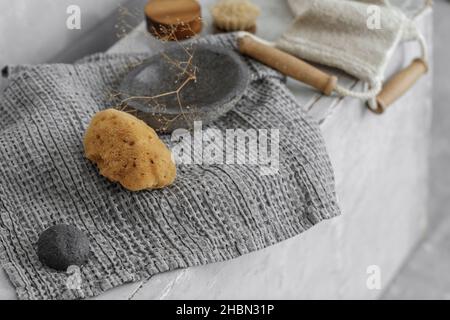 Éponge de mer biologique avec mousse de savon sur plateau en béton gris, crème pour le visage dans un pot avec couvercle en bois, éponge konjac de charbon noir et brosse pour le visage.Accès à la salle de bains Banque D'Images