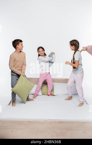 les enfants heureux qui se battent avec un oreiller tout en se tenant isolés sur du blanc Banque D'Images