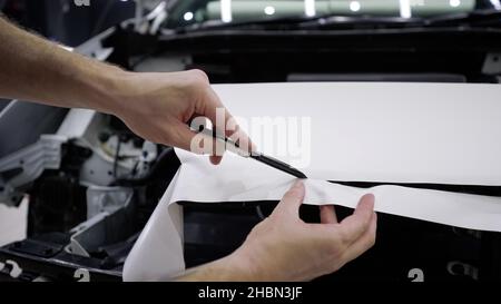 Le gabarit coupe le film sur la machine à l'aide d'un couteau.Rétromontage de la voiture avec un film de protection blanc, le maître effectue une découpe dans le revêtement avec un Banque D'Images