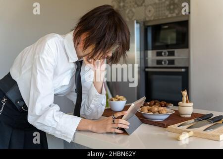 femme exécutive regardant une recette sur une tablette, debout dans la cuisine, image horizontale Banque D'Images