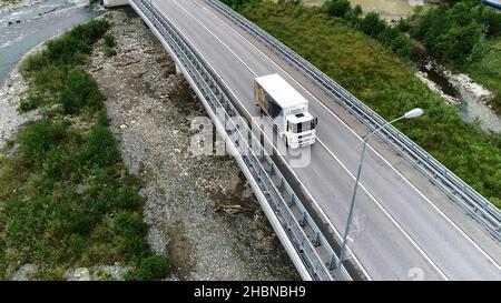 Vue aérienne d'un nouveau pont en béton avec autoroute et conduite de camion blanc, transport de marchandises concept.Camion blanc se déplaçant le long de la forêt verte, vue Banque D'Images