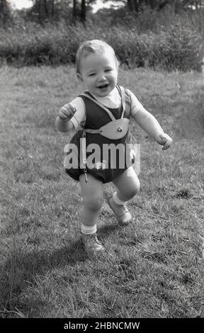 1950s, historique, sur une zone herbeuse, un bébé garçon, hors de son harnais, et sur ses deux pieds appréciant l'air frais, Angleterre, Royaume-Uni. Banque D'Images