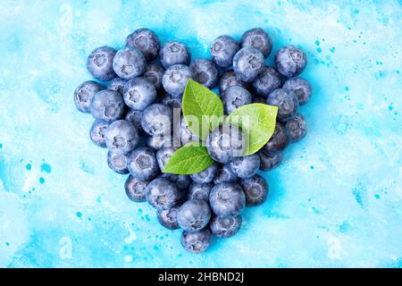 Symbole coeur fait de bleuets mûrs frais et de feuilles vertes sur fond bleu clair aquarelle.Alimentation saine et concept de renforcement de l'immunité. Banque D'Images