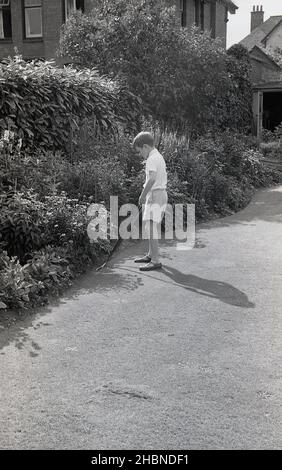 1950s, historique, par une journée ensoleillée dehors dans un jardin, un garçon dans un pantalon court, une chemise à manches courtes et des sandales, aider avec le jardinage, tailler le bord d'une pelouse, à l'aide d'une paire de cisailles à long manche ou sécateurs, Angleterre, Royaume-Uni. Banque D'Images