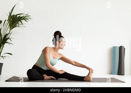 Belle jeune femme s'étirant les jambes sur le tapis de yoga dans Light Studio Banque D'Images