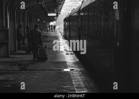 Image en noir et blanc et (noir de film, atmosphérique) avec un homme portant un bagage près d'un train prêt à partir d'une gare sur une blancheur enneigée Banque D'Images