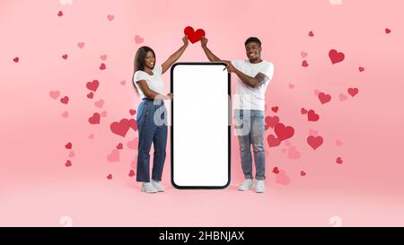 Couple montrant un écran de smartphone blanc vide tenant le cœur en papier Banque D'Images