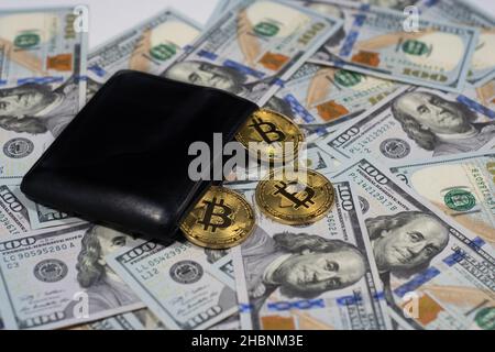 Pièces de monnaie crypto-bitcoin brillantes or avec portefeuille noir sur cent dollars, gros plan Banque D'Images