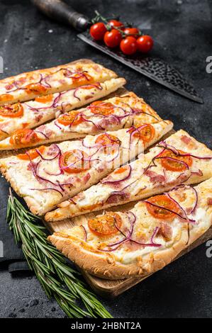 Flamkuchen ou tarte flambee fait maison avec fromage à la crème, bacon, tomates et oignons.Arrière-plan noir.Vue de dessus Banque D'Images