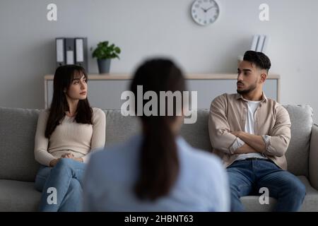 Vue arrière d'une femme psychologue donnant une séance de thérapie à un couple arabe assis sur un canapé et regardant l'un l'autre Banque D'Images