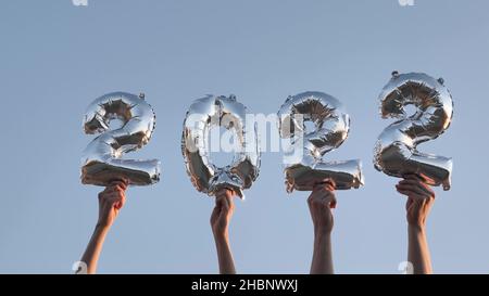 Les mains des gens tiennent de grands ballons d'air en argent en forme de chiffres montrant l'année prochaine contre le ciel bleu sans nuages sur le matin ensoleillé de gros plan Banque D'Images