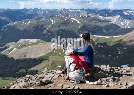 Randonneur femelle assis sur la montagne avec un chien pendant la journée ensoleillée Banque D'Images