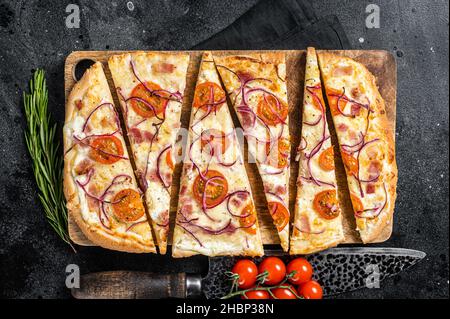 Flamkuchen ou tarte flambee fait maison avec fromage à la crème, bacon, tomates et oignons.Arrière-plan noir.Vue de dessus Banque D'Images