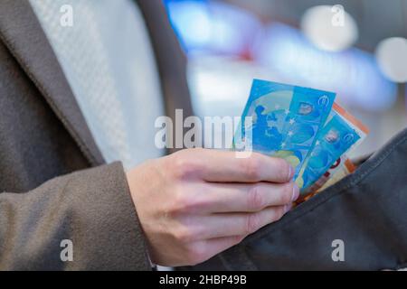 Homme en manteau prend des billets en euros de son portefeuille, la monnaie européenne gros plan dans ses mains Banque D'Images