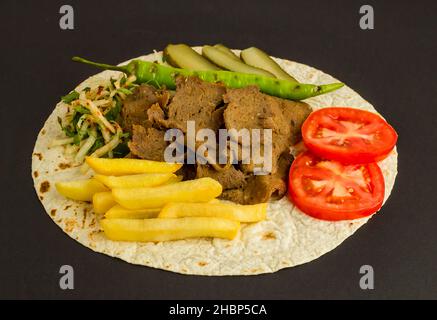 Doner traditionnel turc kebab, servi sur un pain plat, feuille de pain avec tomate, pommes de terre frites, cornichons au concombre et poivre vert grillé. Banque D'Images