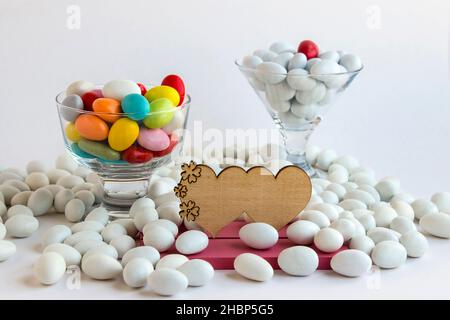 Bonbons traditionnels d'amande blancs et colorés recouverts de turc dans des bols en verre sur une surface blanche avec étiquette en bois vide. Banque D'Images