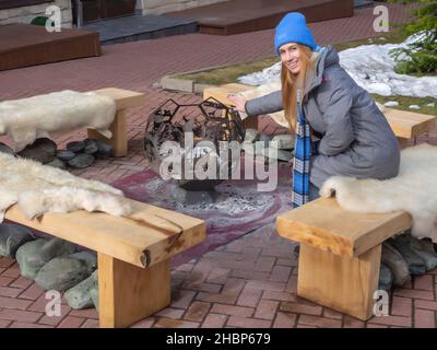 Sotchi, Russie - 25 février 2020.Une fille souriante dans un chapeau bleu tient sa main sur un brazier décoratif sous forme de balle tout en étant assise sur un banc Banque D'Images