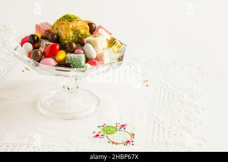 Pâtisserie turque traditionnelle dessert une tranche de Baklava sèche conçue avec des bonbons colorés dans un bol en verre sur un tissu en dentelle fait à la main et un espace de copie Banque D'Images