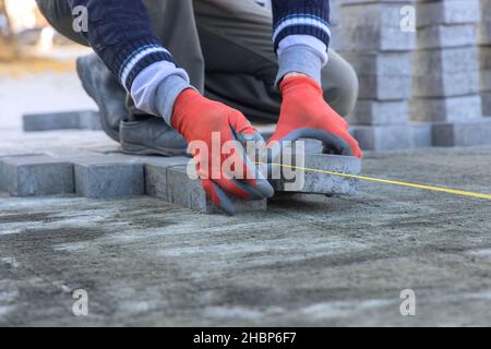 Gros plan de l'ouvrier de construction qui pose des briques de ciment sur le trottoir Banque D'Images