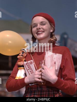 Jeune femme ado en queue de cochon vêtue d'une tenue rouge et d'un chapeau de béret rouge assorti tenant les Cracker Jacks, le pop-corn et le ballon jaune dans un cirque Banque D'Images