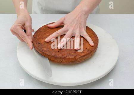 La femme coupe le gâteau au chocolat en deux couches.Gâteau au chocolat étape par étape avec une recette de glaçage à la crème au chocolat Banque D'Images