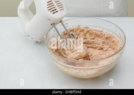 La recette de glaçage au gâteau au chocolat.Mélangez le beurre, la vanille et la poudre de cacao dans un bol en verre près de la table de cuisine Banque D'Images