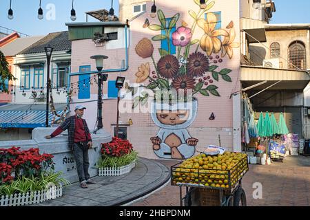 Un marchand de fruits se détend par un pont au-dessus de Klong (canal) ONG Ang dans la région de Phahunat/Chinatown à Bangkok, en Thaïlande, dans les maisons colorées et une murale Banque D'Images